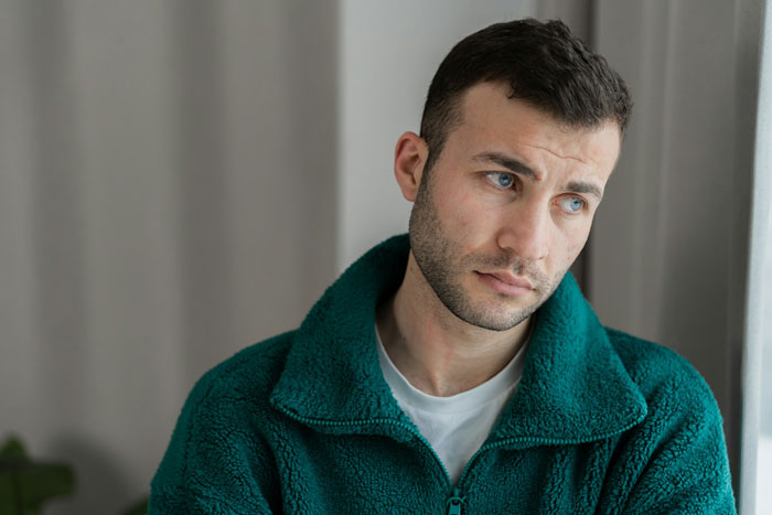 Young man in a teal fleece looking upset and contemplative, reflecting on family conflicts involving parenting and siblings.