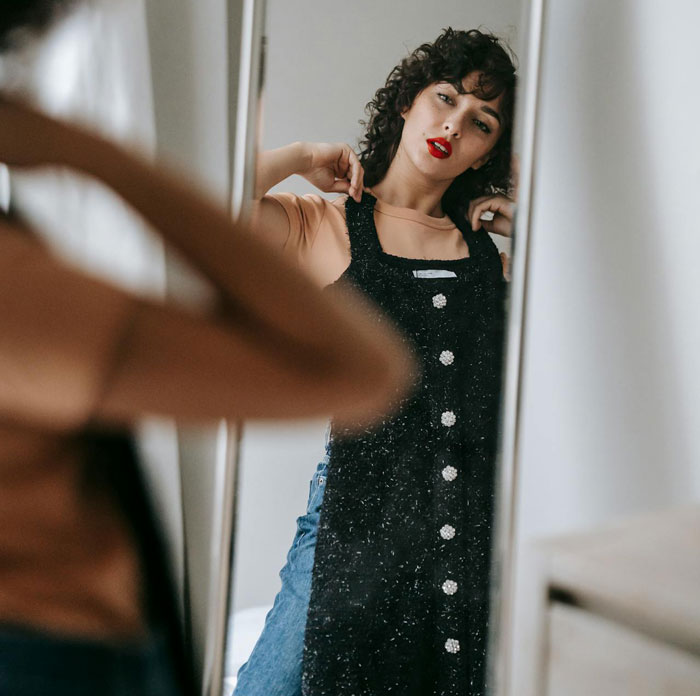 Woman looking frustrated in mirror, holding dress, reflecting emotions related to parenting and family conflict.