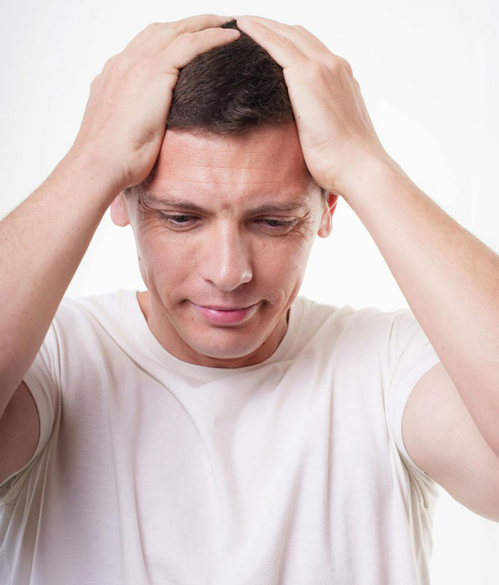 Stressed man in white shirt holding his head, depicting tension from woman going berserk over parenting and sibling meddling.