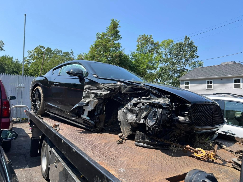 A severely damaged black car on the back of a flatbed tow truck.