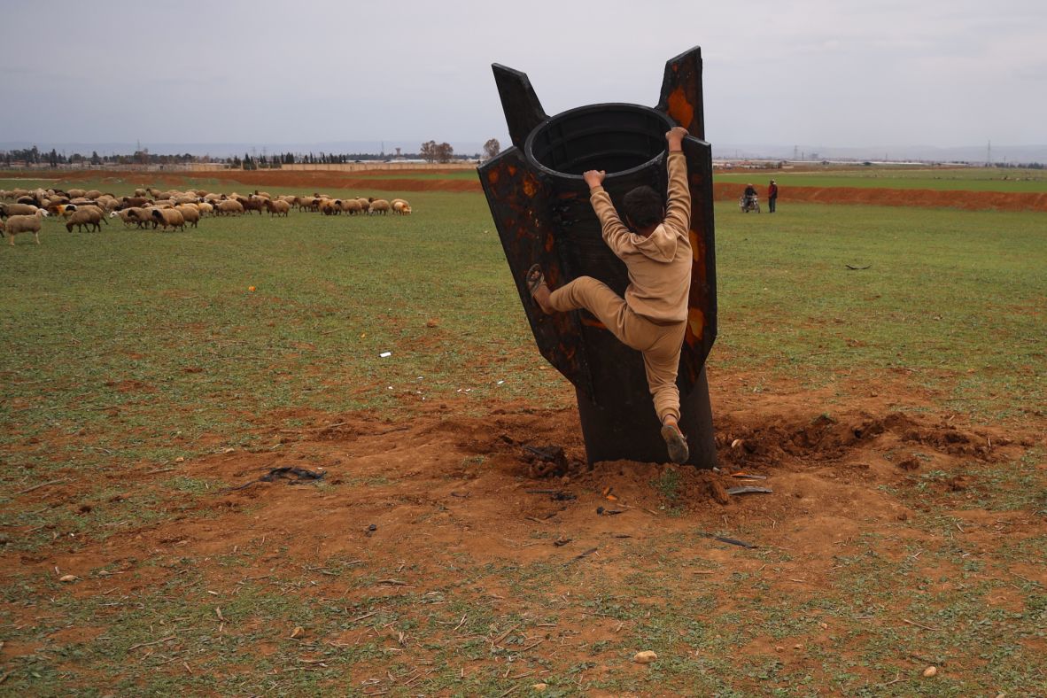 A boy tries to climb on an unexploded missile after it fell in an open field in Qamishli, Syria, on Wednesday, March 4.