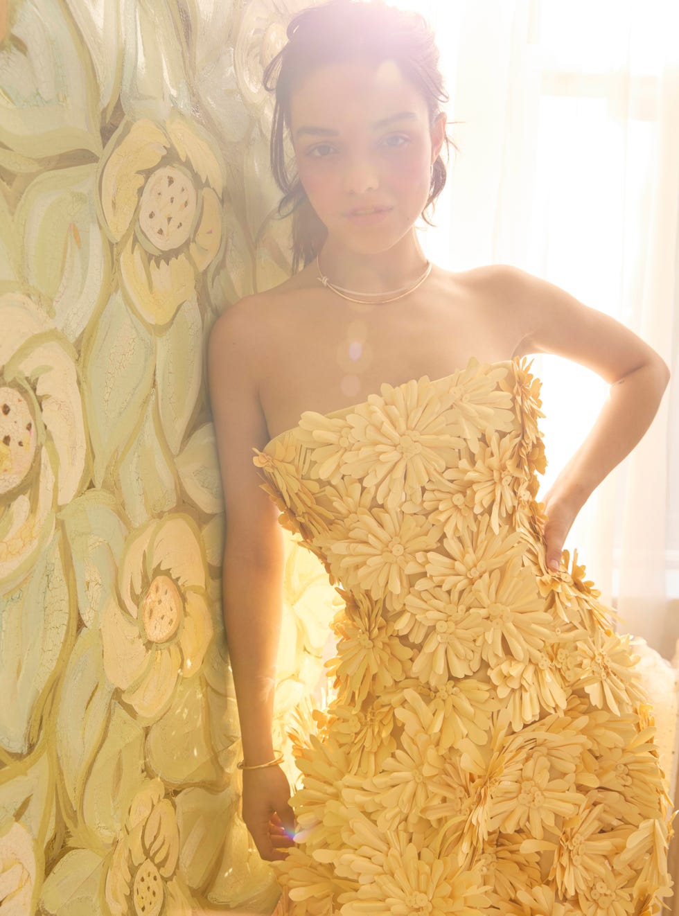 woman in a floral yellow dress leaning against a wall