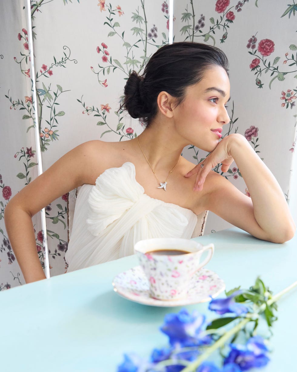 a woman in a white dress near a coffee cup and blue flowers