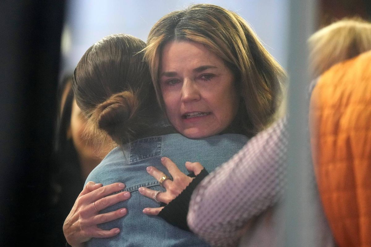 An adult woman is embracing a young girl in a comforting manner while standing in an indoor setting.