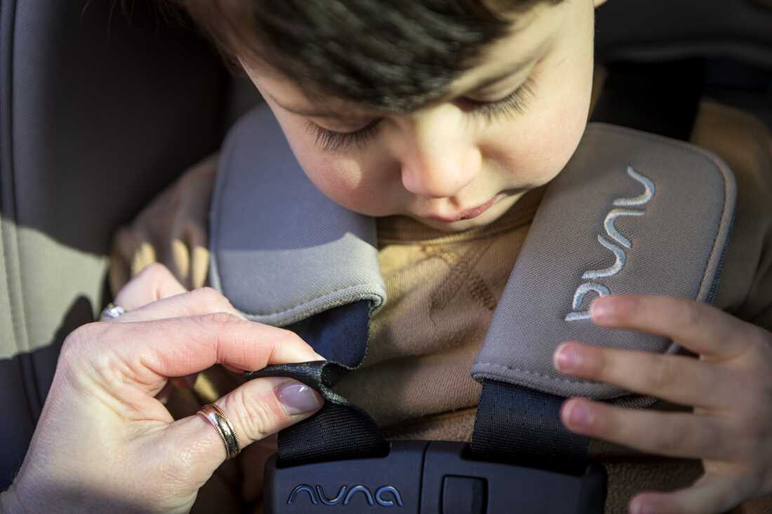 Kanagawa pinches the webbing of the harness on a car seat while a young boy sits in the seat. Being able to pinch the webbing means the harness is too loose, she says.