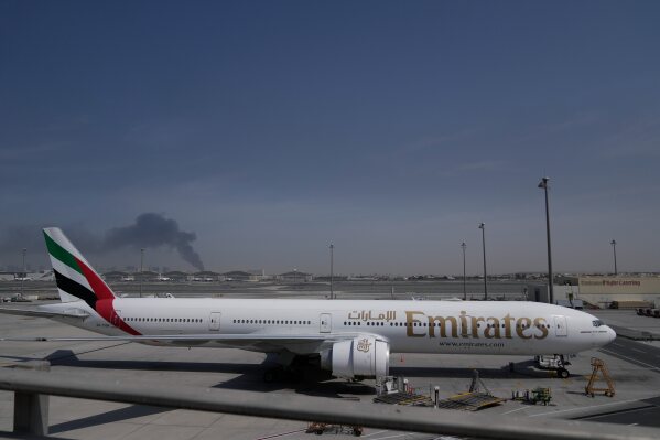 ADDS CAUSE OF BLACK SMOKE IN THE BACKGROUND.- A plume of smoke caused by an Iranian strike is seen in the background an an Emirates plane is parked at the Dubai International Airport after its closure in Dubai, United Arab Emirates, Sunday, March 1, 2026. (AP Photo/Altaf Qadri)