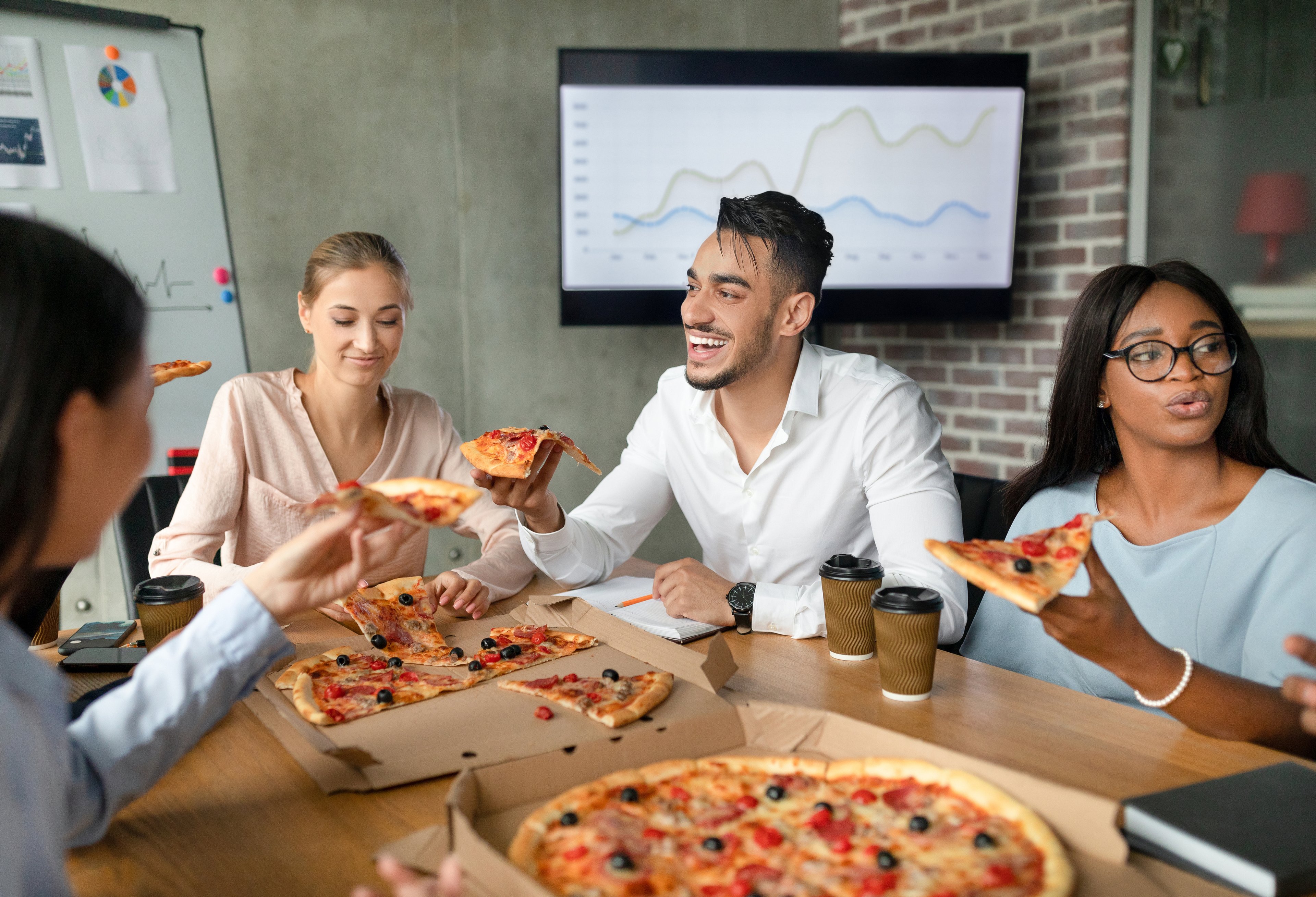 Employees eating pizza while seated at a large table in a conference room.