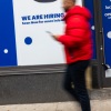 A person walks past a storefront with "we are hiring" and "opening soon" signs out front.