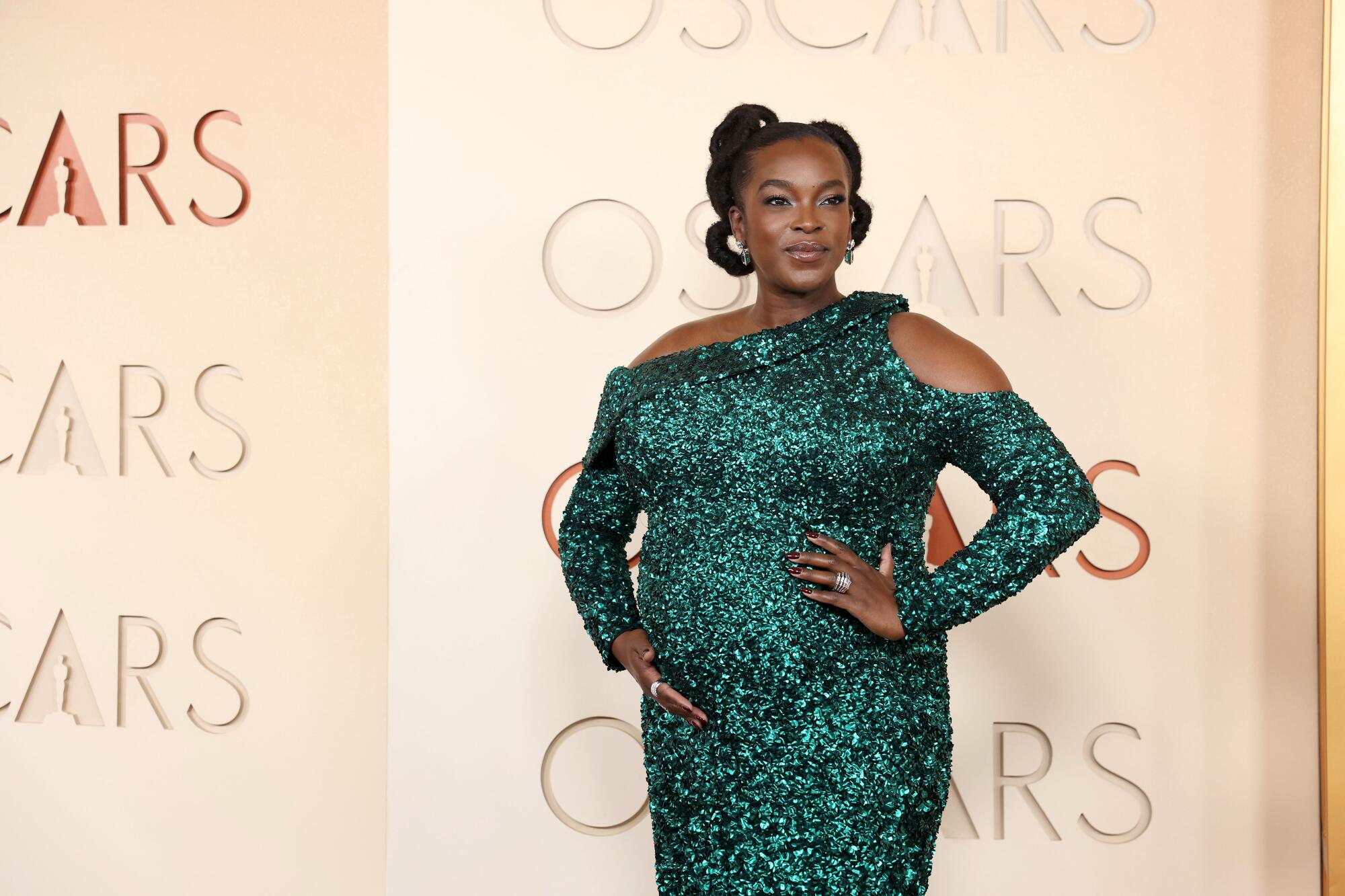Wunmi Mosaku, wearing a sequin green dress, poses on the red carpet. 