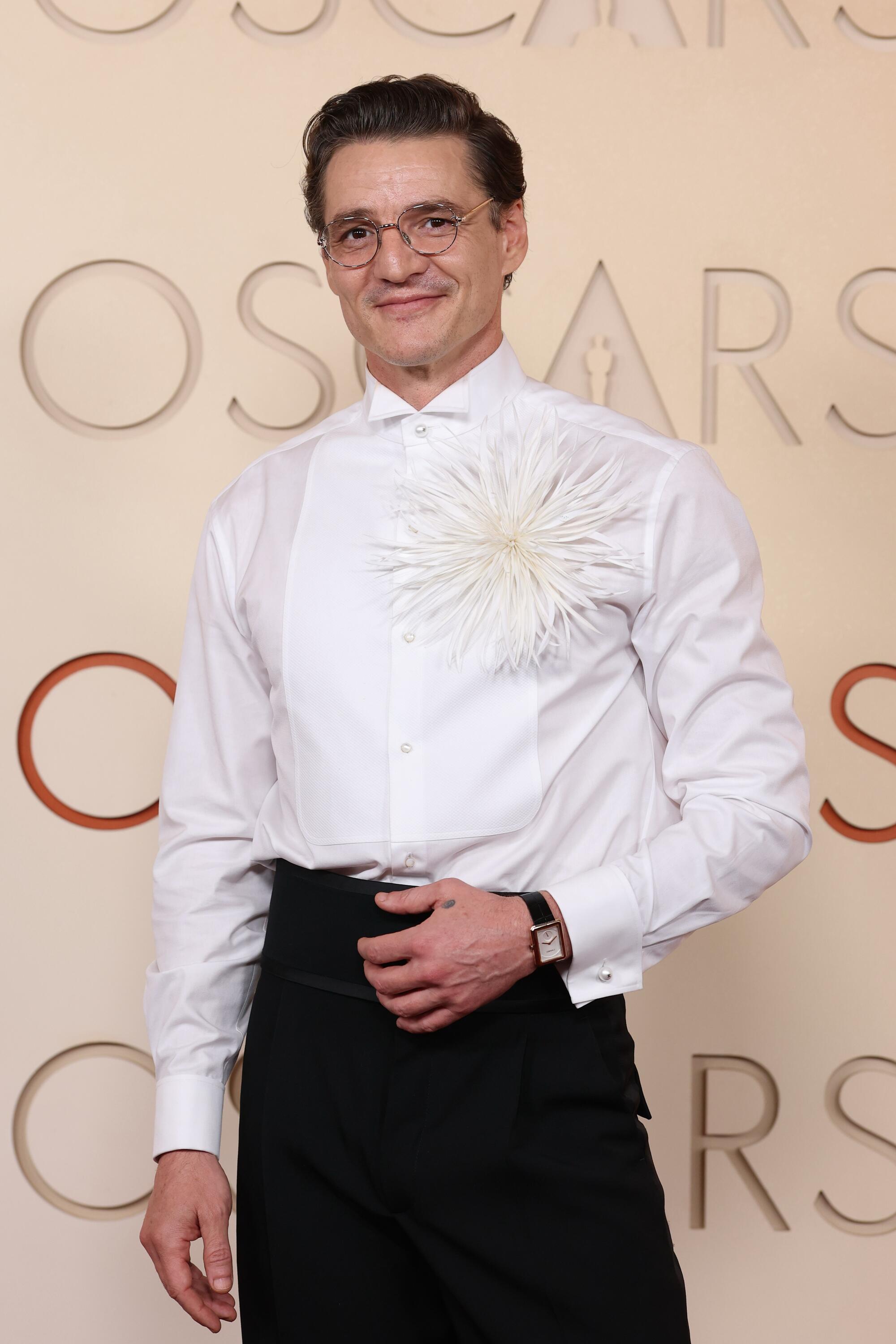 Pedro Pascal, wearing a white shirt with a huge brooch, poses on the red carpet. 