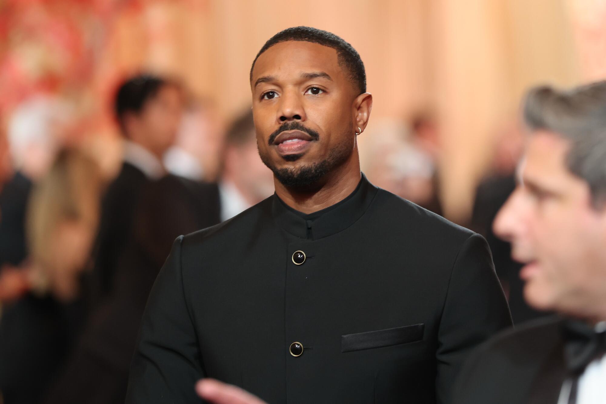 Michael B. Jordan, wearing an all-black suit, walks on the red carpet. 