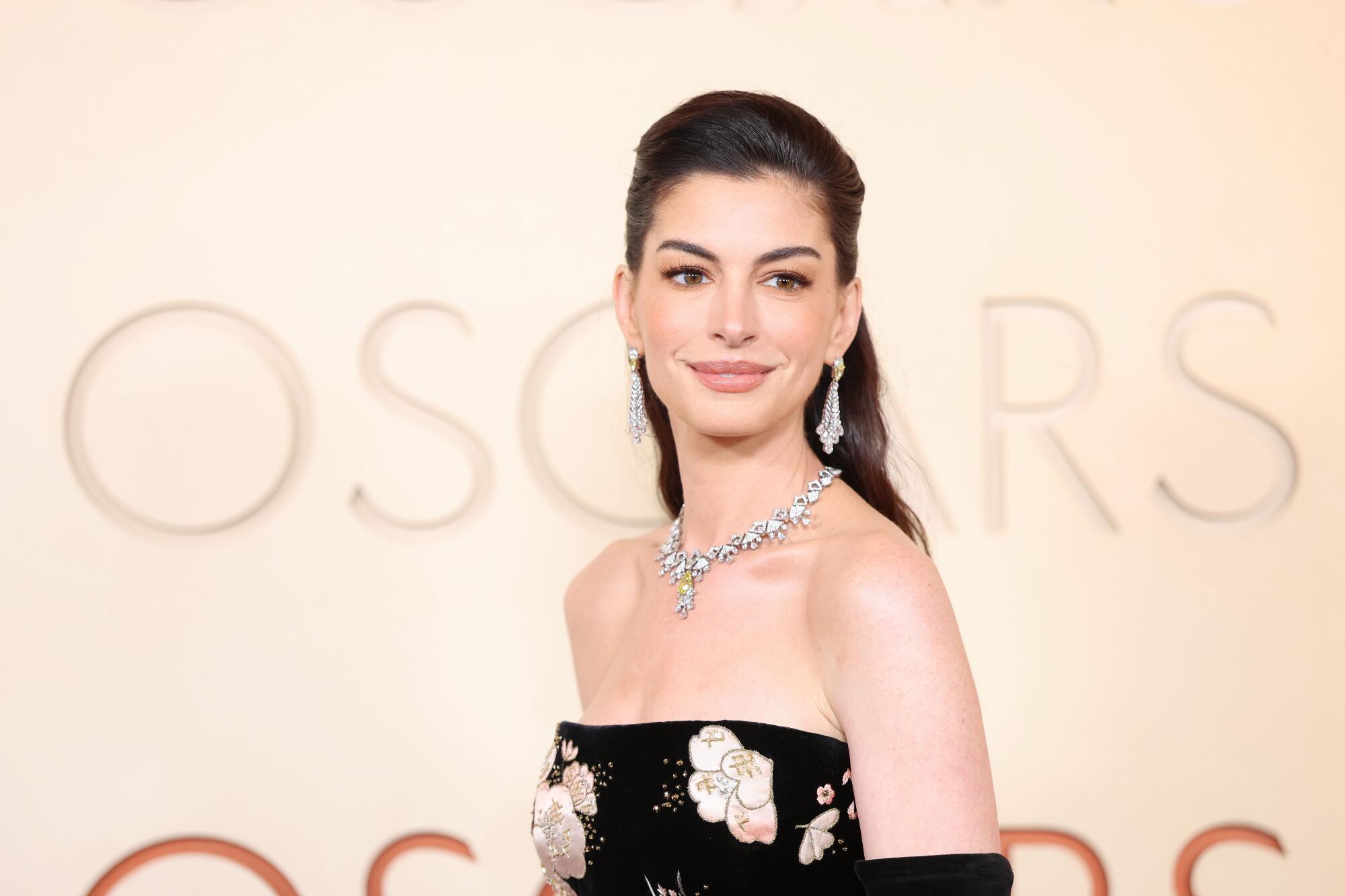 Anne Hathaway, wearing a black dress with floral embroidery, poses on the red carpet. 