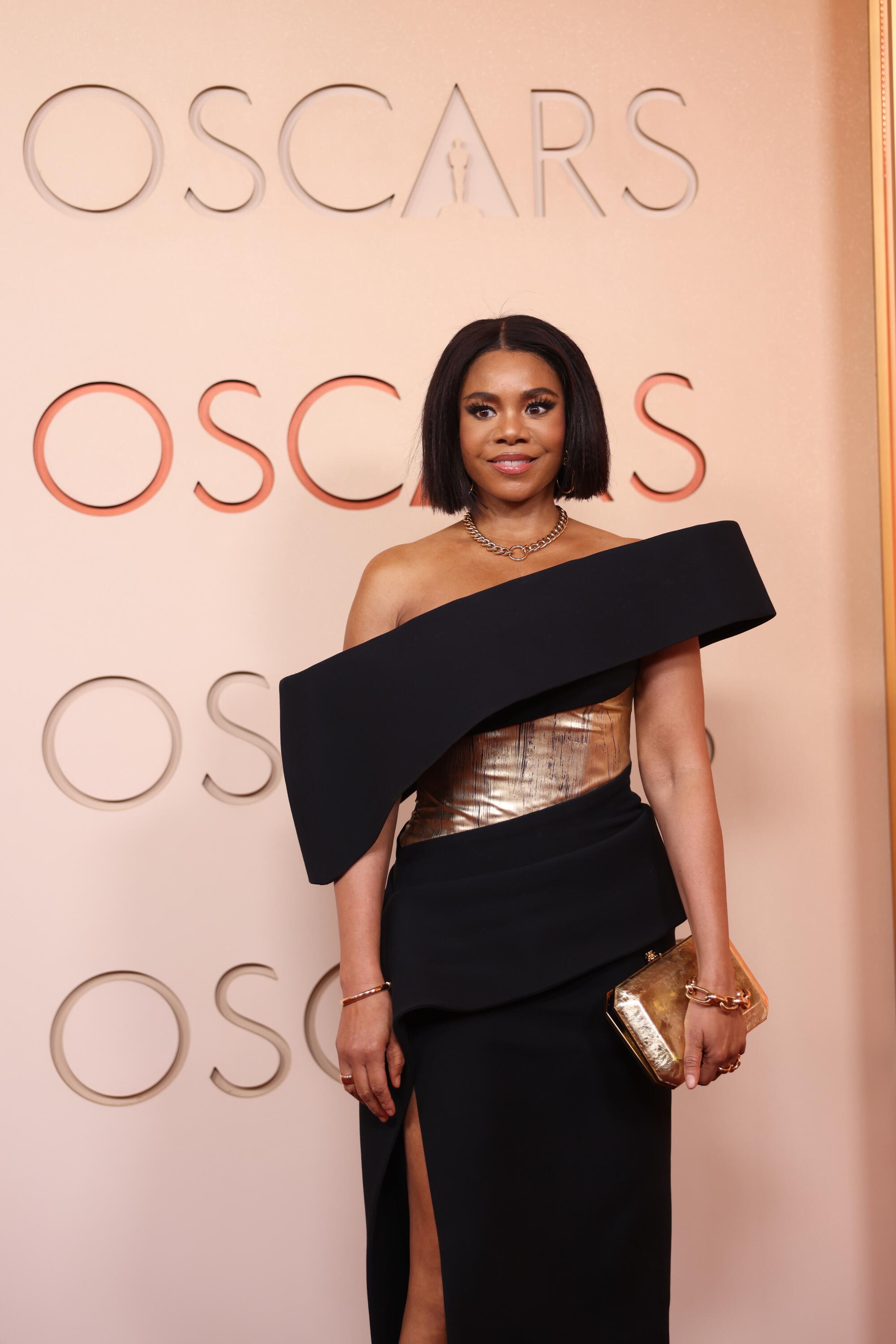 Regina Hall, wearing a black and gold dress, poses on the red carpet. 