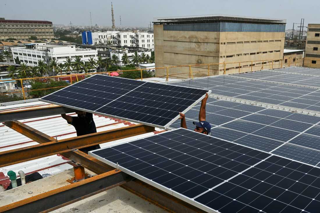 In this photograph taken on July 2, 2025, technicians install solar panels on the rooftop of a factory in Pakistan's port city of Karachi.