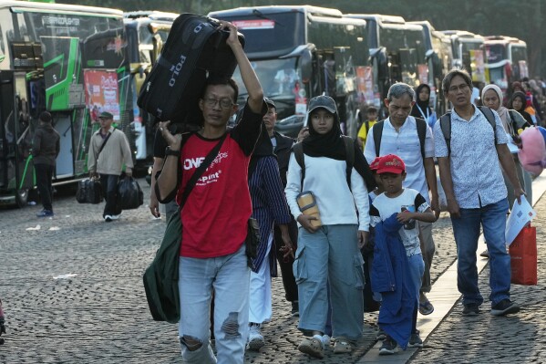 People carry their belongings as they arrive for a free bus trip to their hometowns organized by the Jakarta provincial government in Jakarta, Indonesia, Tuesday, March 17, 2026. The annual exodus out of the capital and other major cities in the world's most populous Muslim country is underway as millions of Indonesians are leaving for their home villages to be with their family members to celebrate Eid-al Fitr, the holiday marking the end of the Muslim fasting month of Ramadan. (AP Photo/Achmad Ibrahim)