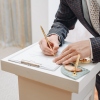 A young man standing at wedding ceremony and signing wedding documents, groom in black costume, cropped, unrecognizable.