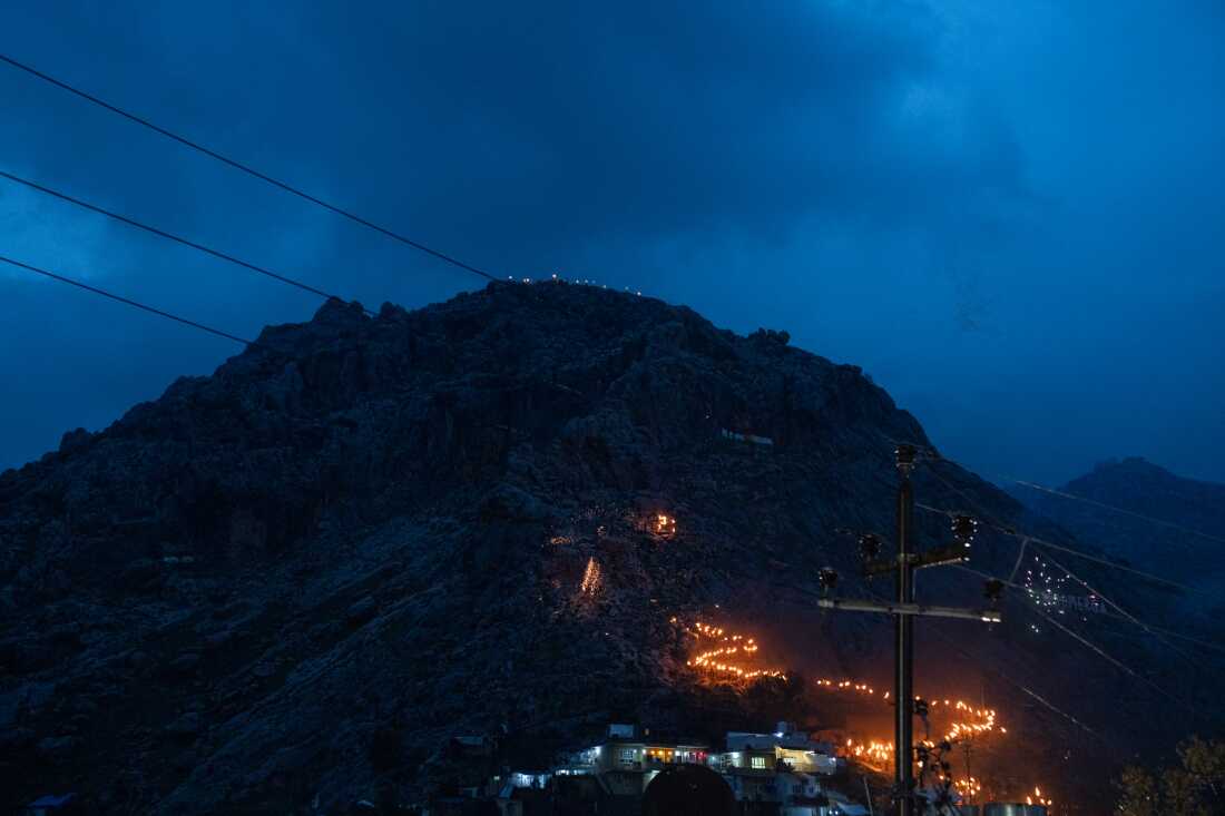 A view of flaming torches being carried about a third of the way up a mountain at twilight.