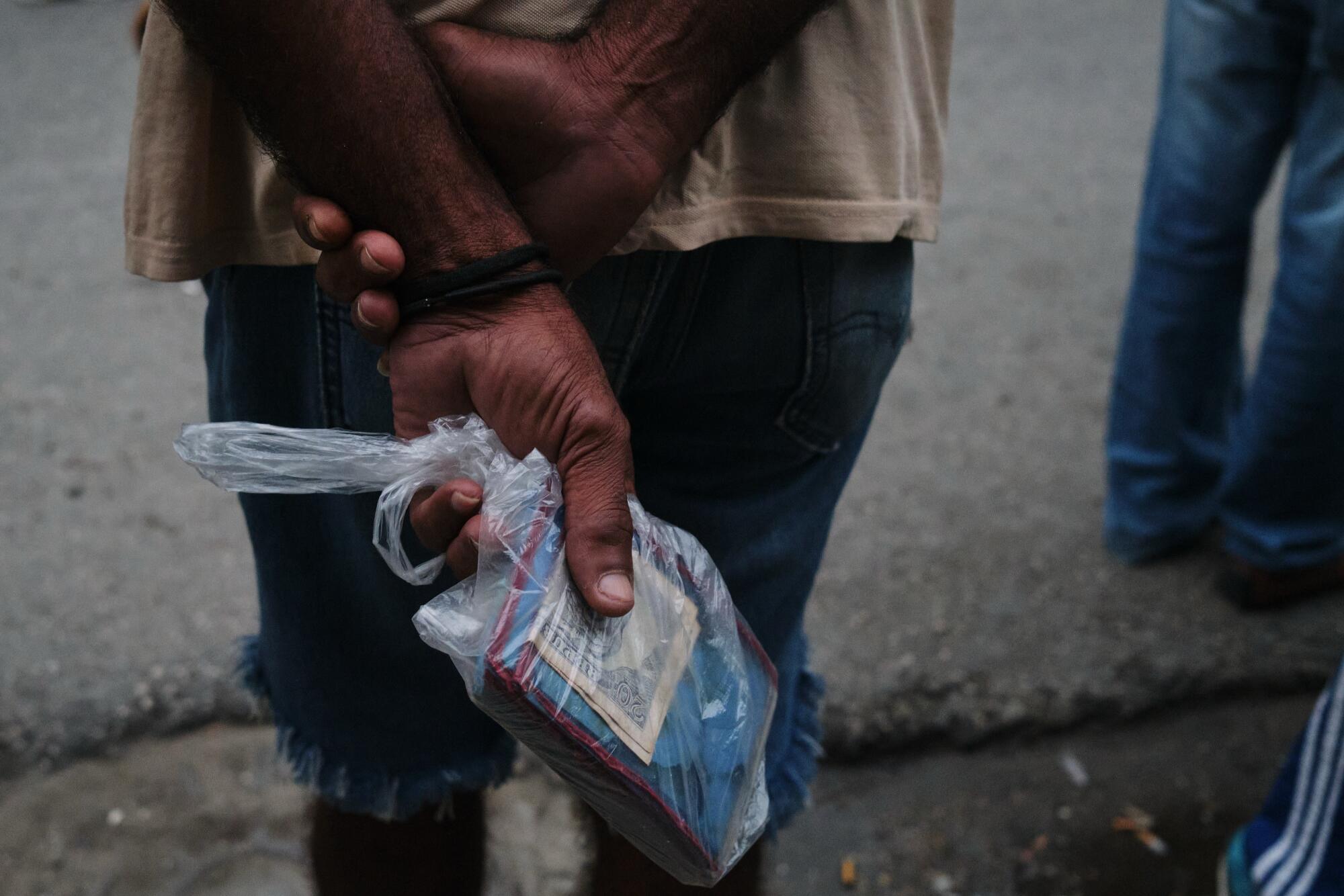 A man holds a booklet and cash wrapped in a small plastic bag.