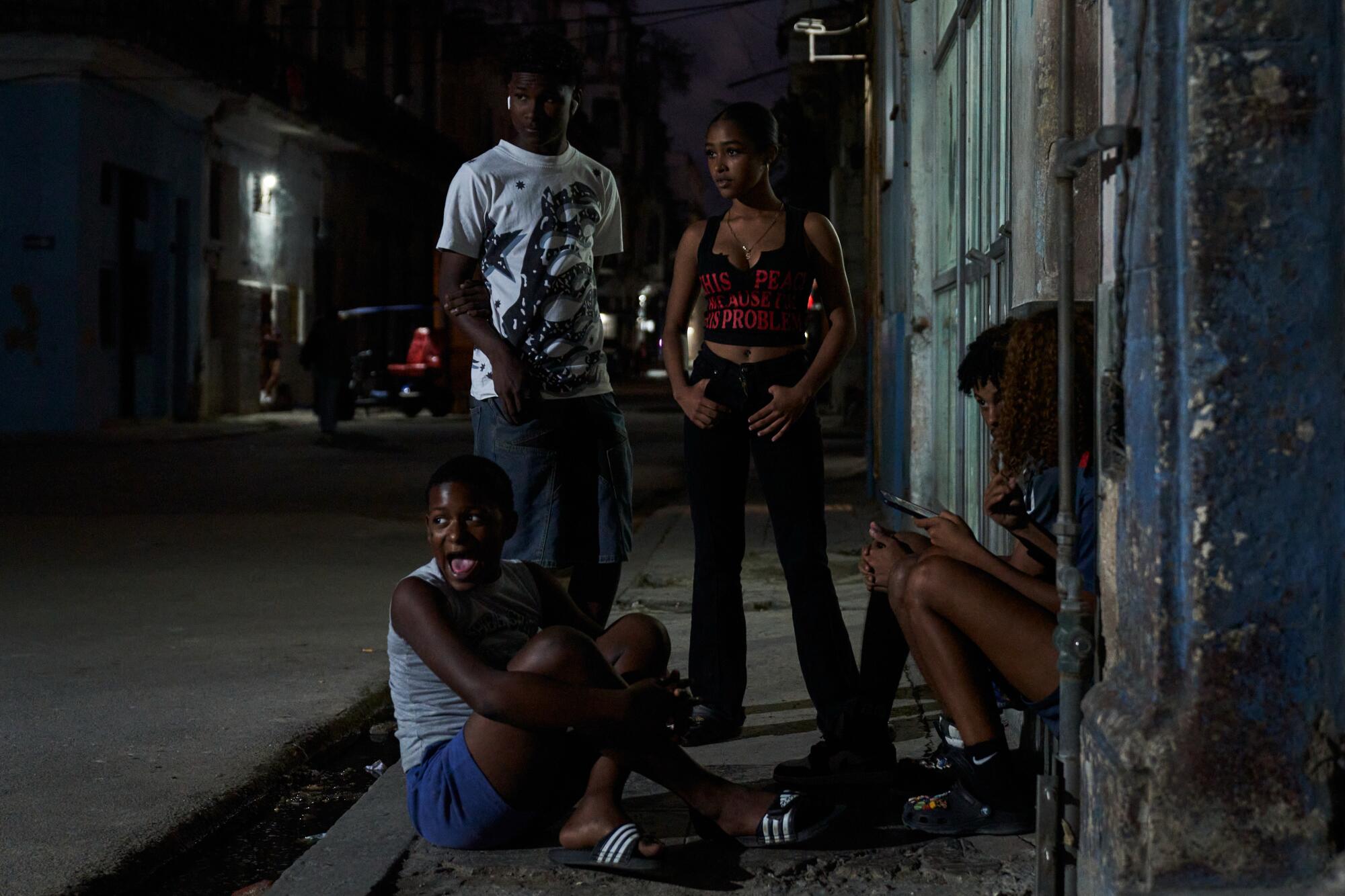 Four young people stand and sit in a dark street.