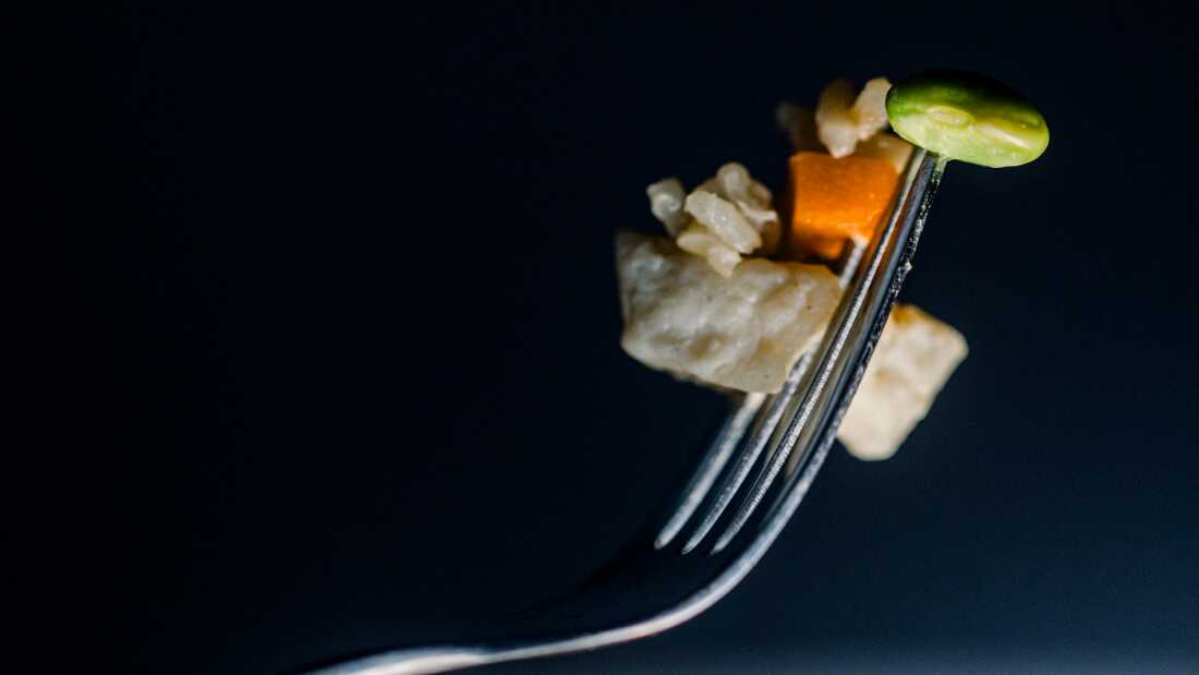 A close up photo shows a bit of chicken, rice, carrot and edamame on a fork.