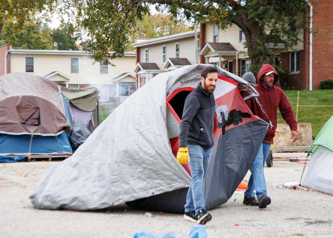 A Home Sweet Home Ministries employee and a volunteer drag a tent to a dumpster in a church parking lot that was being used as a homeless encampment.