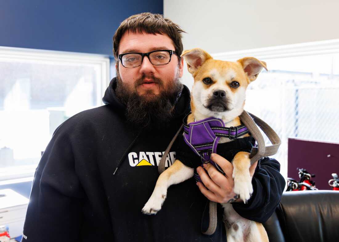 Matthew Stone, one of the first residents of The Bridge, stands with his dog, Tank, inside the shelter village’s community center.