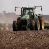 A green tractor that's planting corn moves across a brown dirt field in 2007 near Rochelle, Illinois.