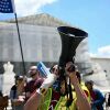 Protesters stand outside the U.S. Supreme Court. One holds a flag, another has a bullhorn, and some hold signs.