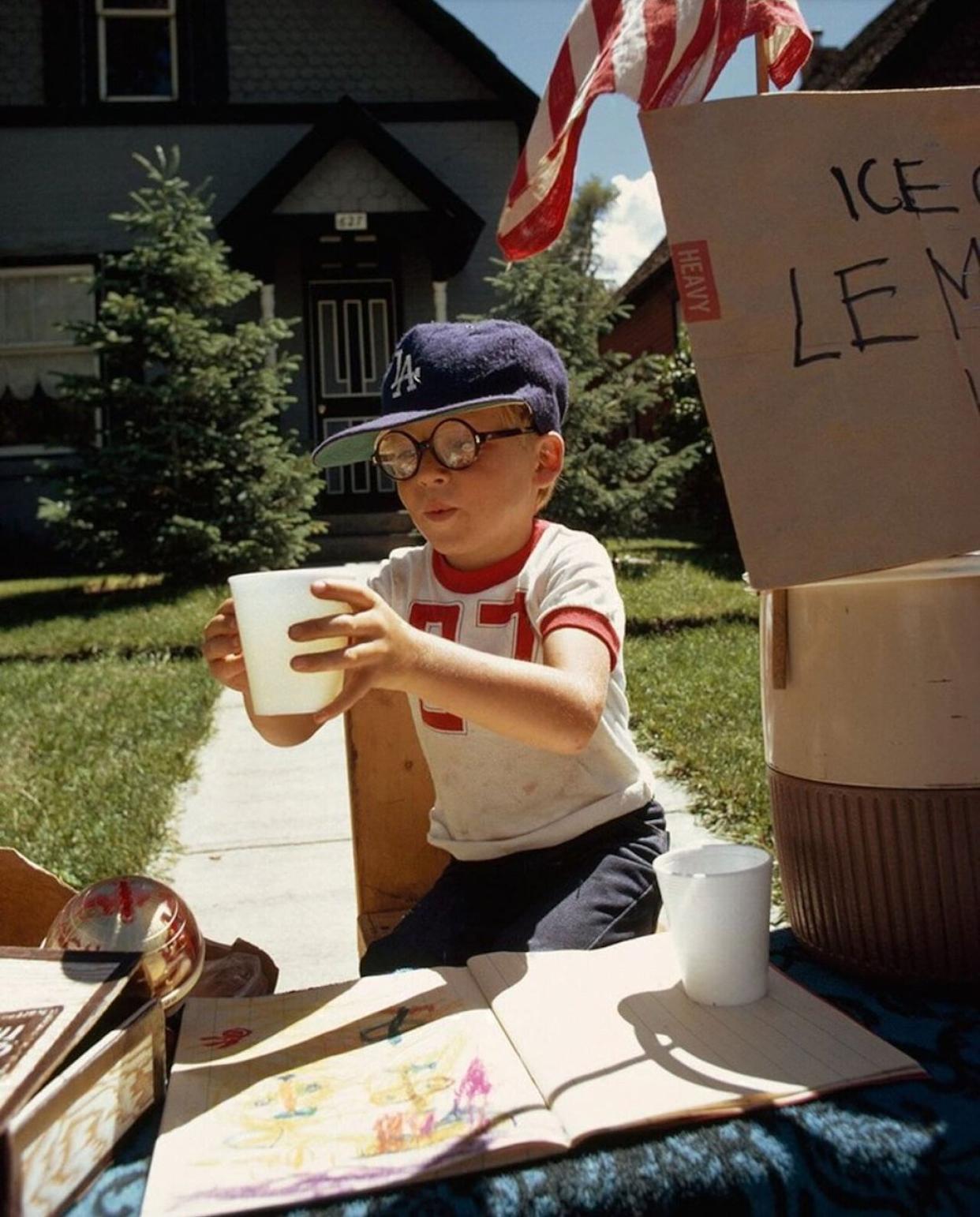 A boy wearing a Dodgers ball cap selling lemonade in his front yard -