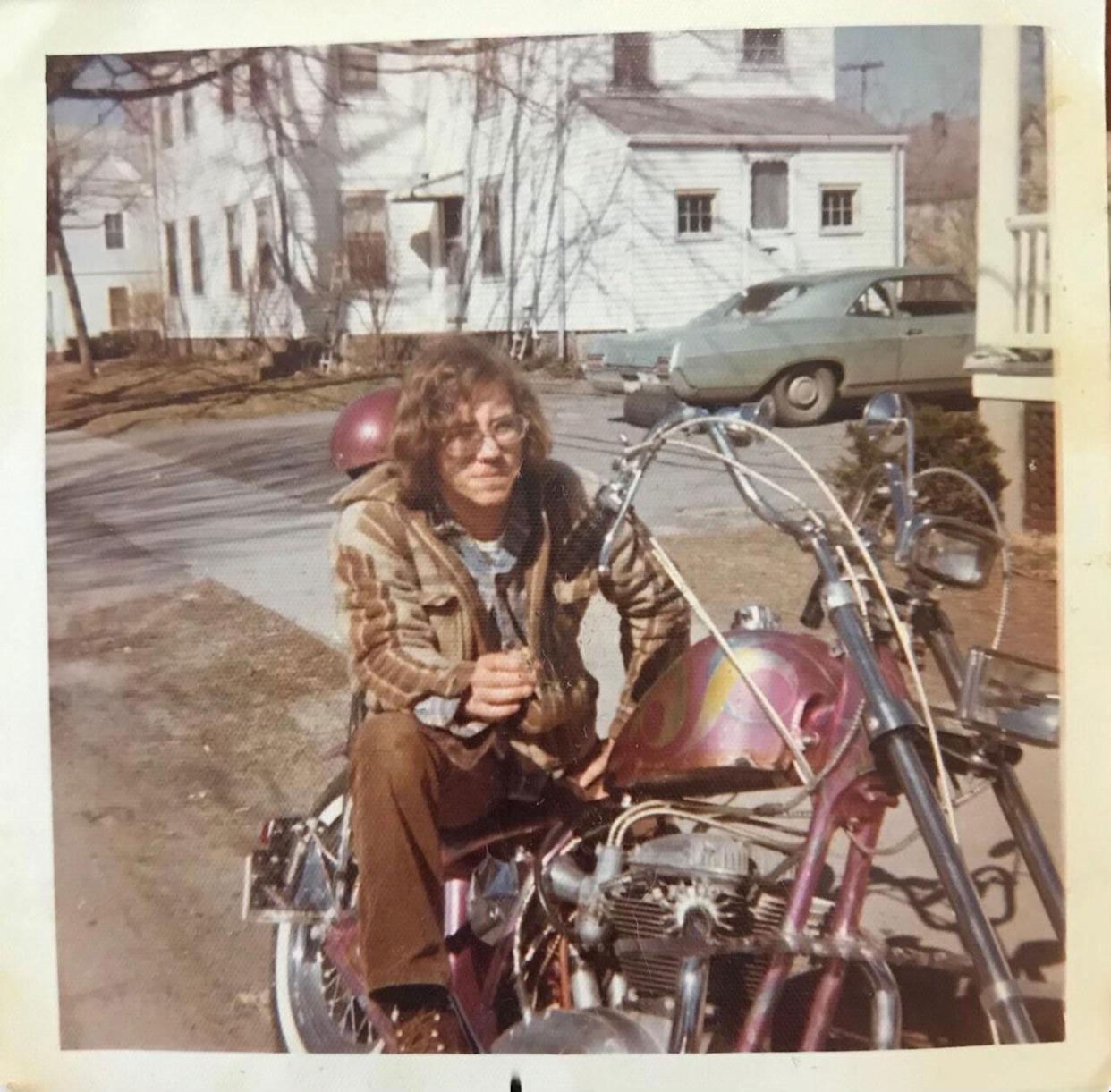 A young man sits on a pink motorcycle in a driveway -