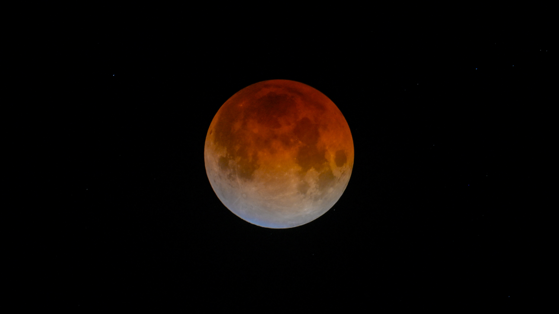 A red full moon is shown during an eclipse, with a part of its lower edge bathed in a soft blue light.