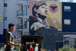 Pedestrians walk below an image of Cesar Chavez on a mural in San Francisco, Wednesday, March 18, 2026.
