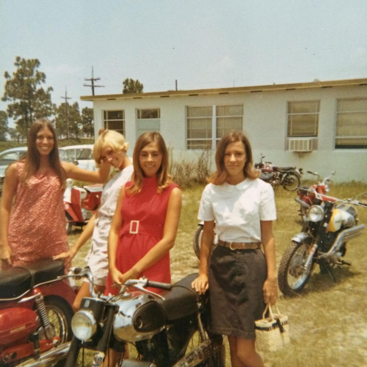 A group of young woman smiling and standing around their motorcycles -