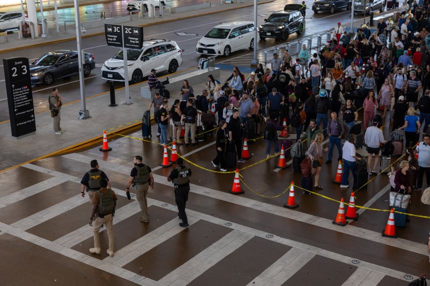 Immigration and Customs Enforcement agents pass by as travelers wait in line outside of Terminal E at George Bush Intercontinental Airport Friday in Houston, Texas.