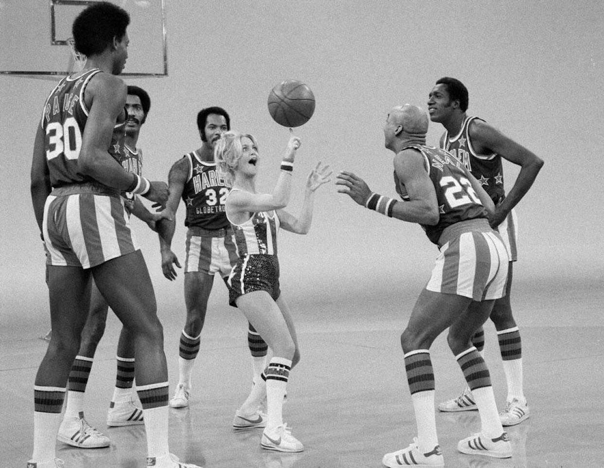 Black and white photo of Goldie Hawn spinning a basketball on her finger, surrounded by the Harlem Globetrotters -