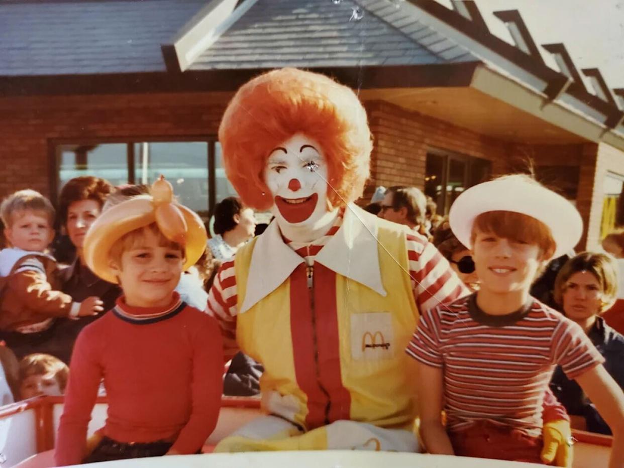 Two boys sitting on either side of a man dressed as Ronald McDonald -