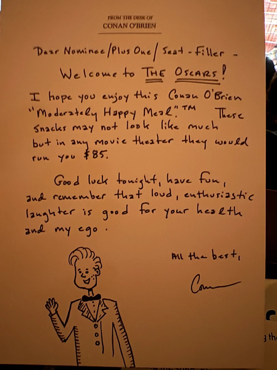 Printed card titled 'From the Desk of Conan O’Brien' with a handwritten welcome note to Oscars nominees and a cartoon drawing of Conan waving.