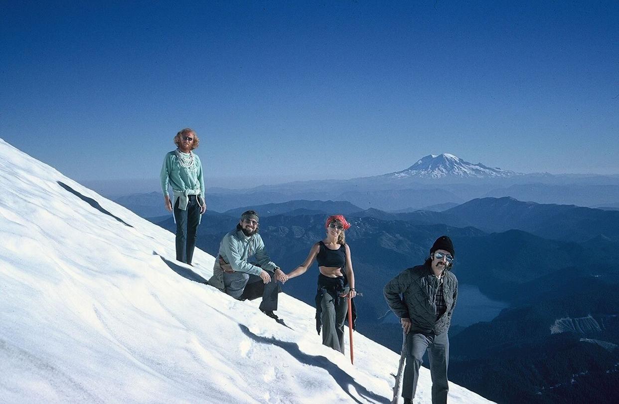 Four people standing on a snowy mountainside with mountain in the distance -