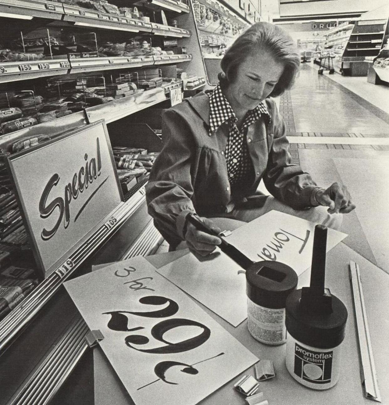 Woman sitting at a table in a grocery store painting the sale signs -