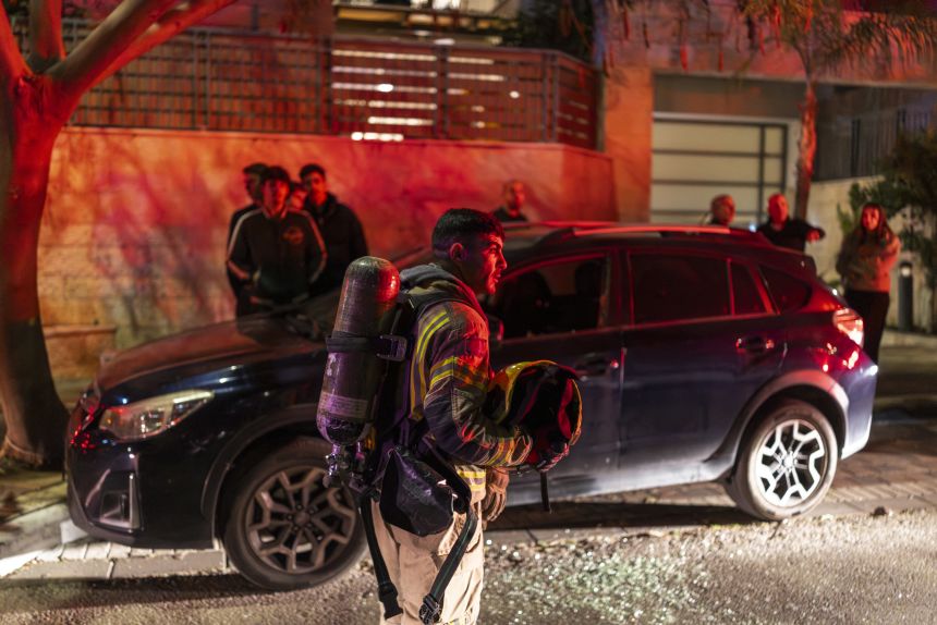 A firefighter holds a helmet as he operates outside a building hit by a projectile in a city in outskirts of Tel-Aviv, Israel, on March 6, 2026.