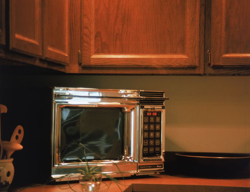 An Amana chrome Radarange microwave oven sits on a kitchen countertop in the 1970s.