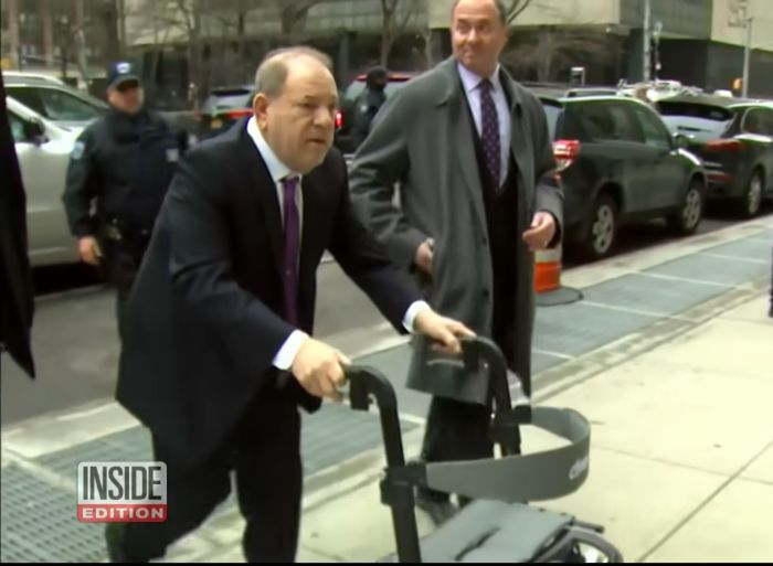Harvey Weinstein using a walker outside a courthouse with security and a man in a gray coat nearby