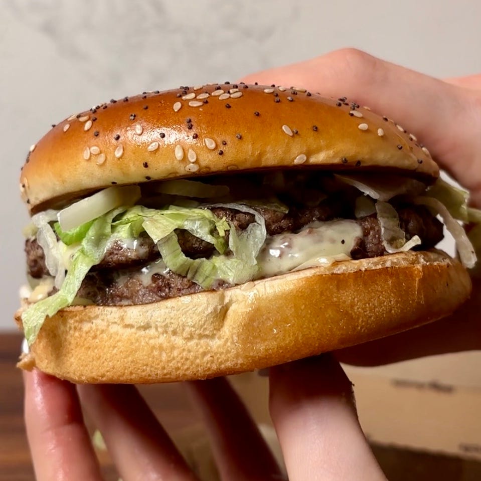 hand holding a hamburger with sesame seed bun