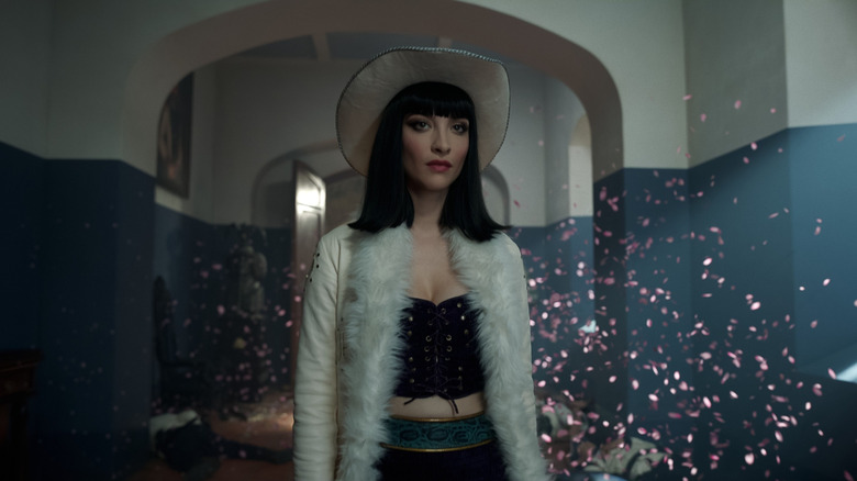 Lera Abova as Miss All Sunday with a white jacket on and glitter in the background in One Piece season 2