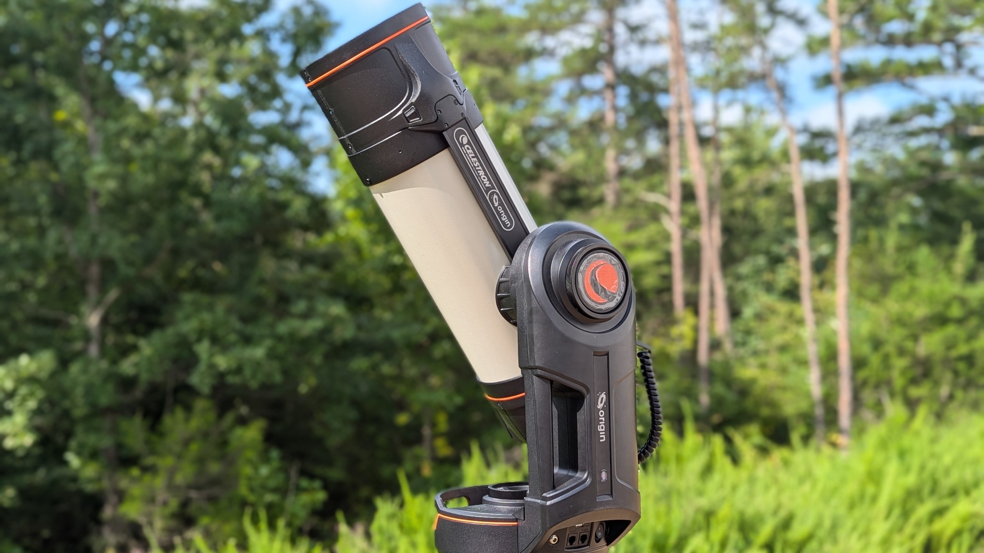 a black and white telescope in a field with trees behind it