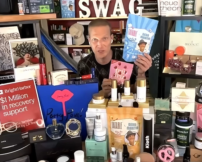 Man presenting an elaborate $346K Oscars gift bag for nominees with various luxury beauty and wellness products.
