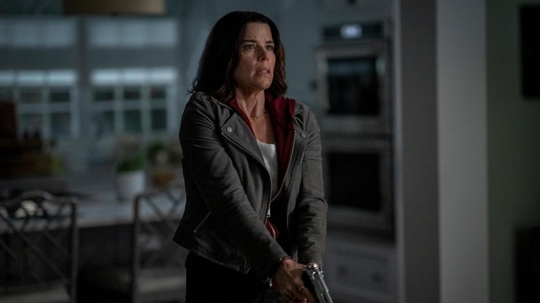 Neve Campbell as Sidney Prescott holding a gun in her kitchen in Scream 7