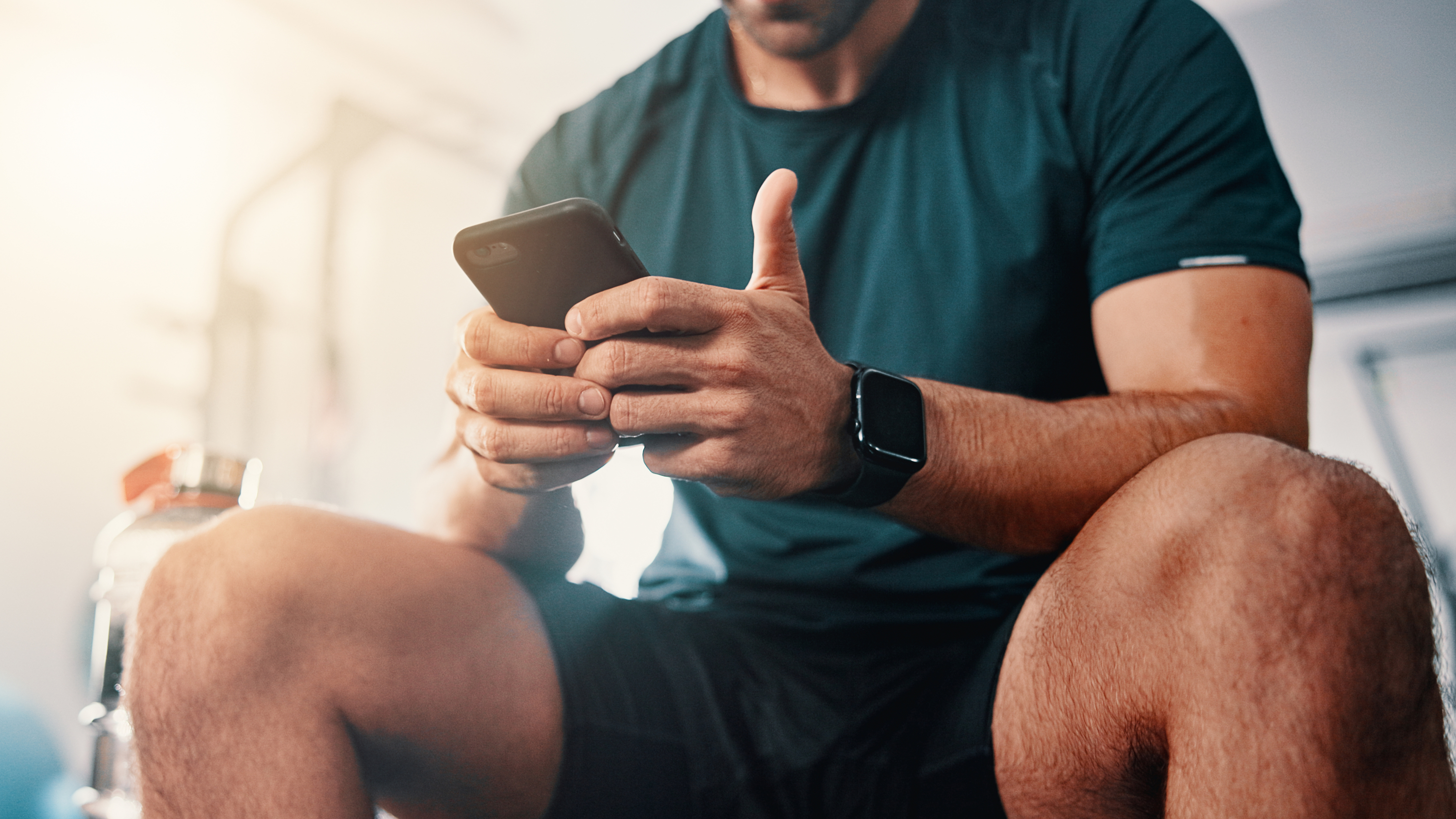 a man in gym gear sat down and looking on phone