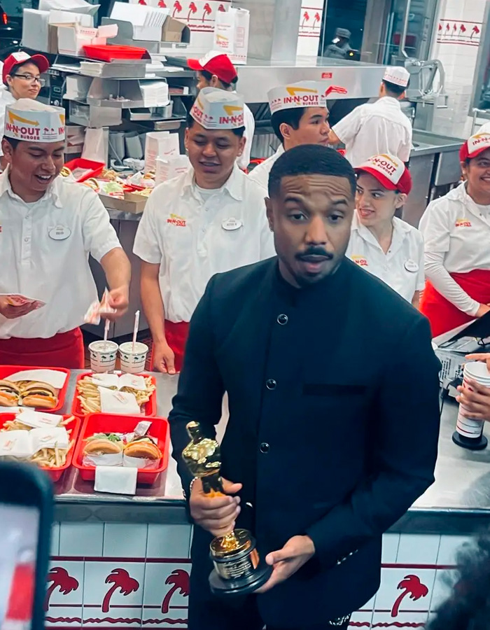 Michael B. Jordan holding an Oscar trophy inside a fast food restaurant surrounded by employees in uniform.
