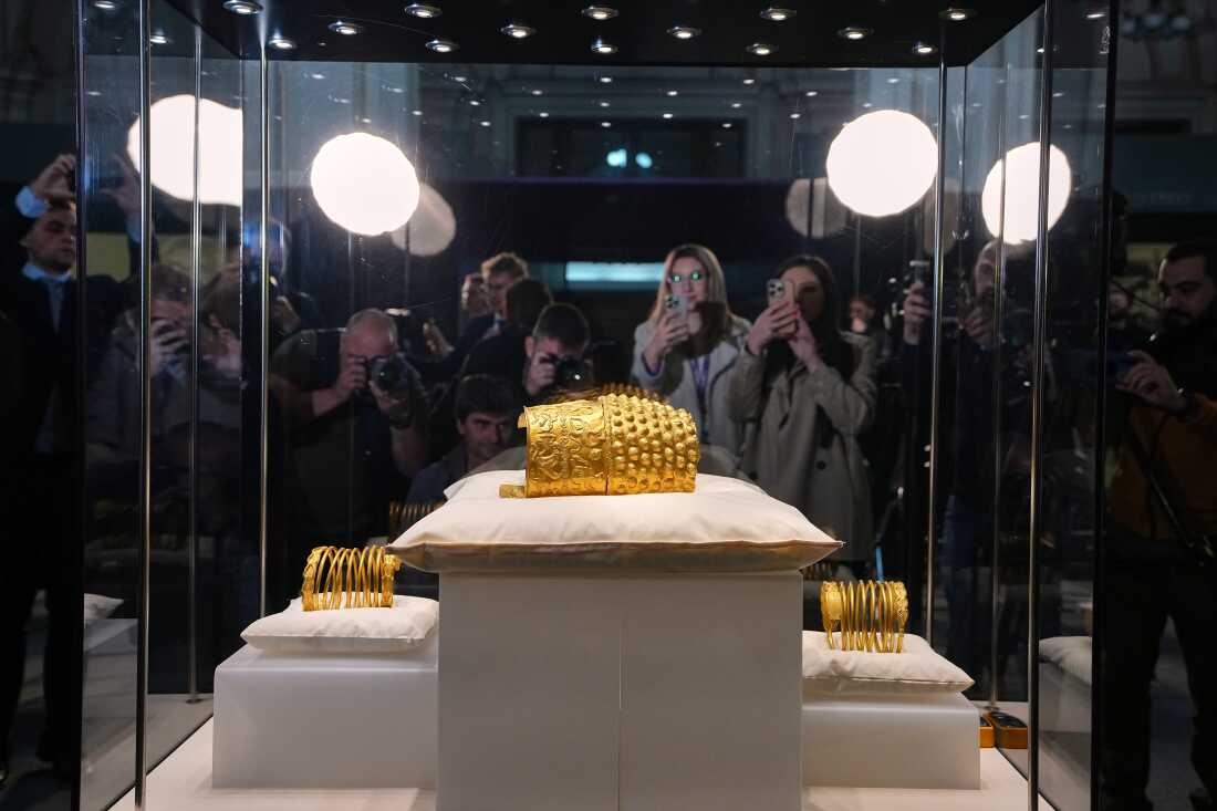Journalists gather around a glass enclosure with the Dacian gold items, a 2,500-year-old helmet and wristbands, stolen from a museum in the Netherlands and then recovered by Dutch authorities, after they were presented upon being returned at the National Museum of Romanian History, in Bucharest, Romania, Tuesday, April 21, 2026.